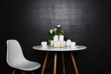 A white coffee table with white cups and tea pot, white candles, some green grass and flowers. accompanied by a white chair. loft design