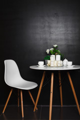 A white coffee table with white cups and tea pot, white candles, some green grass and flowers. accompanied by a white chair. loft design