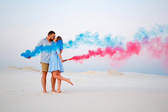 young couple kissing and holding colored smoke in hands, romantic couple with blue color and red color smoke bomb on beach.