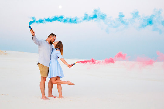 young couple kissing and holding colored smoke in hands, romantic couple with blue color and red color smoke bomb on beach.