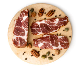Three pieces of fresh meat on a wooden plank with black pepper and pecan nuts on a white background.