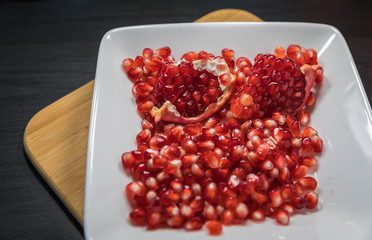 Delicious pomegranate seeds placed in glass jar with fresh organic pomegranates on rustic wooden background.Close up,Copy space