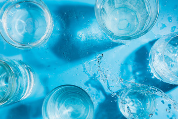 Flatlay arrangement with splashing sparkling water in various glasses , summer drink concept. Top view, Blue background, selective focus
