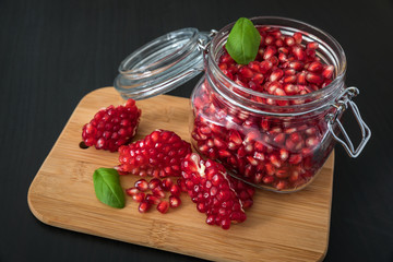 Delicious pomegranate seeds placed in glass jar with fresh organic pomegranates on rustic wooden background.Close up,Copy space