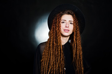 Studio shoot of girl in black with dreads and hat at black background.