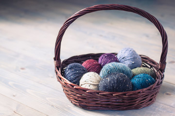 Colorful balls of wool yarn in a basket on the rustic background