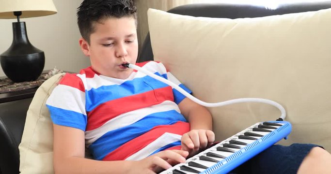 Portrait of a happy schoolboy playing melodica at home