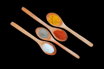 Several spices in wooden spoons isolated on black background.