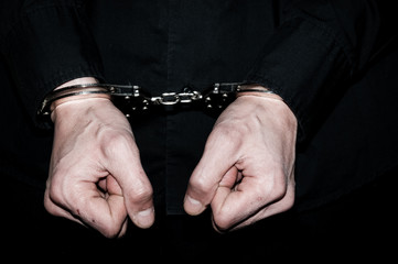 Handcuffs on hands of a arrested handcuffed criminal man in black shirt.