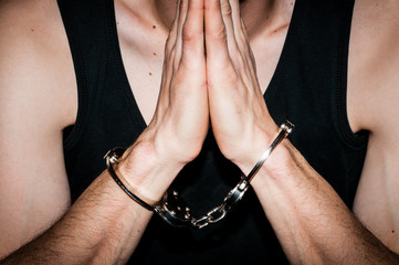 Prayer arrested criminal man with handcuffs on his handcuffed hands pray to God.