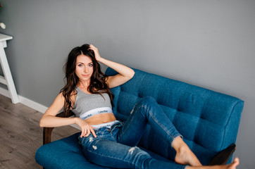 beautiful young girl lies on the couch in blue jeans and a short T-shirt. A girl is resting at home