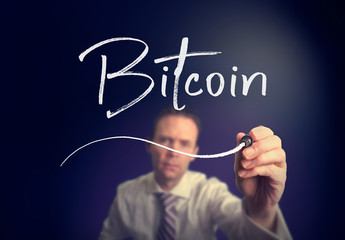 A businessman writing a Bitcoin concept with a white pen on a clear screen.