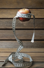  an apple tied with a centimeter, suspended in the air on a wooden background
