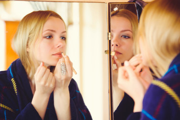 cute blonde woman doing make-up at home, touching face dressed in blue dress, beautiful portrait in house, simple home picture