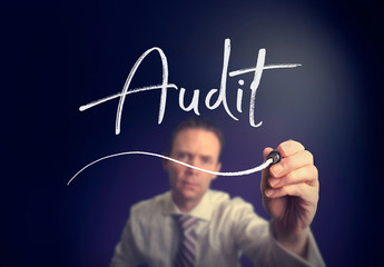 A businessman writing a Audit concept with a white pen on a clear screen.