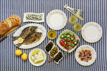 Freshly cooked seafood grilled sea bream fishes, octopus in vinegar sauce, sardines in olive oil and vegetable salad, olives, feta cheese, bread, white wine served for two persons.