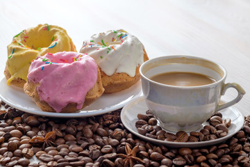 Three baked cupcakes with icing and cup of coffee with milk on light table. Near it scattered coffee beans. Close-up view.