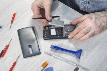 Dłonie serwisanta wyjmują baterie z telefonu komórkowego leżącego na blacie. 
