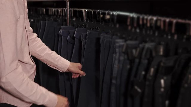 Close up shot of a man looking for a decent pair of jeans in shop. He is taking different pairs and checking them.