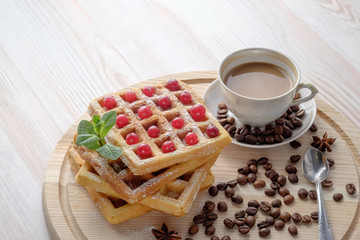 The cup of coffee with milk and stack of Belgian waffles with cranberries, sprinkled of powdered sugar on light cutting board. Copy space for your text.