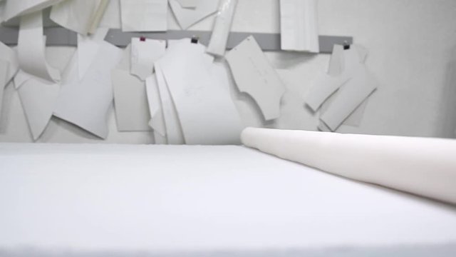 Clothing designer is working with measurements on a studio table. Shot on in 4K UHD . Closeup deploy a skein of white fabric in white and light-colored sewing in slow motion.
