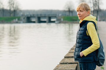 Pretty blonde tourist woman standing near river in park.