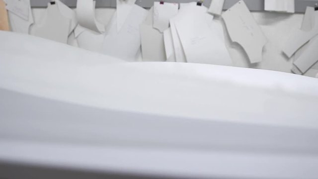 Clothing designer is working with measurements on a studio table. Shot on in 4K UHD . Closeup deploy a skein of white fabric in white and light-colored sewing in slow motion.