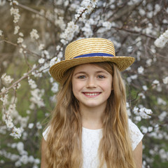 Pretty little girl in hat walking in blossom cherry garden on beautiful spring day