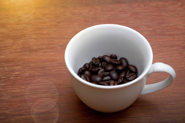 Coffee beans in white cup put on wooden floor.