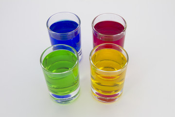 Multicolored glasses of different drinks. Party and holiday celebration concept. Four glasses with a blue, green, yellow and red drink. Isolated on white background.