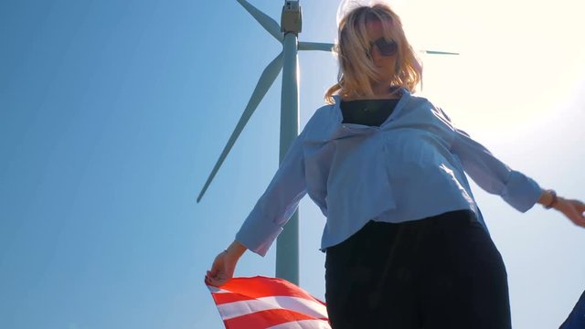 Native American girl with flag with stars and stripes near giant windmills in the field. Love to your country. Celebrating 4th July Independence Day. 4K in slow motion. American dream.