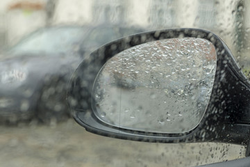 Drops of rain on the car window (glass) with a view of the exterior mirror and blurred background
