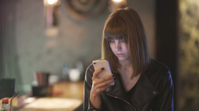 young beautiful red-haired woman sitting in cafe or bar and using a smartphone