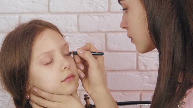 Makeup to the child. To the little girl, the older sister makes an eye makeup.