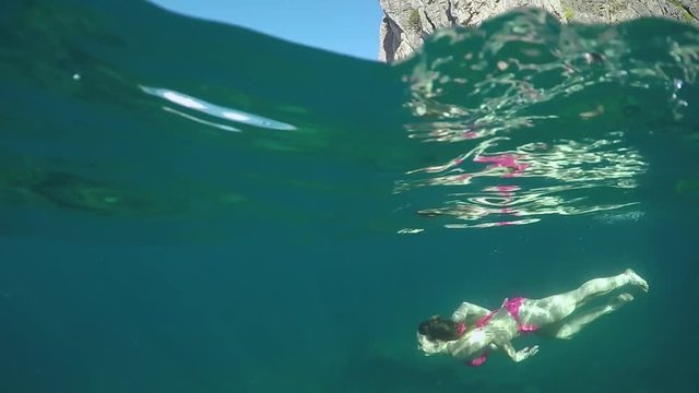 SLOW MOTION, HALF UNDERWATER: Cheerful young woman dives in deep sea on a beautiful summer day in Krabi. Carefree girl on relaxing holiday swims in picturesque scenery with clear sky and large cliffs.