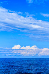 Fototapeta na wymiar Panoramic view of ocean waters horizon line with dramatic cumulus thunderstorm cloudscape in blue sky background.