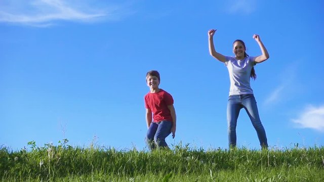 Happy kids jumping together on green grass hill against blue sky