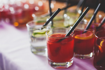 Beautiful row line of different colored alcohol cocktails on a party,  on decorated catering bouquet table
