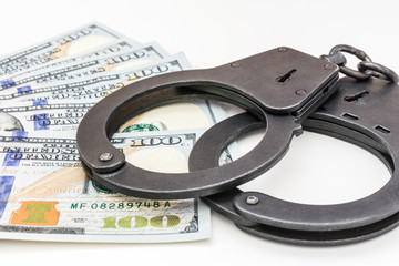 black metal handcuffs lying on the 100 dollars banknotes on a white background