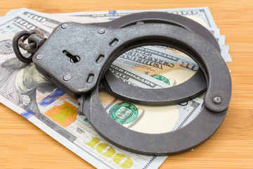 black metal handcuffs lying on the 100 dollars banknotes