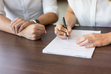 Close-up of female hands filling in questionnaire at job interview. Young Caucasian businesswoman sitting at table with male partner and signing contract. Job interview and signing contract concept