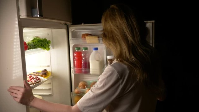 Woman opens the refrigerator at night. night hunger. diet. gluttony, 4k