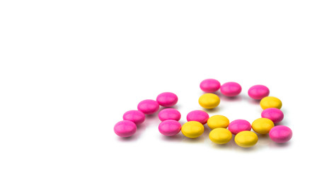 Pile of pink and yellow round sugar coated tablets pills isolated on white background with copy space. Colorful pills for treatment anti-anxiety, antidepressant and migraine headache prophylaxis.