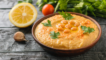 Freshly made hummus in a clay brown bowl on a rustic table with a piece of bread.