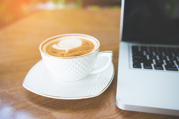 Cup of coffee and laptop on wooden table.