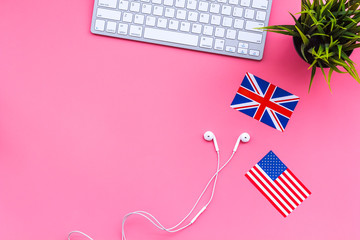 Learn english online. Computer keyboard, headphones, british and american flags on pink background top view copy space