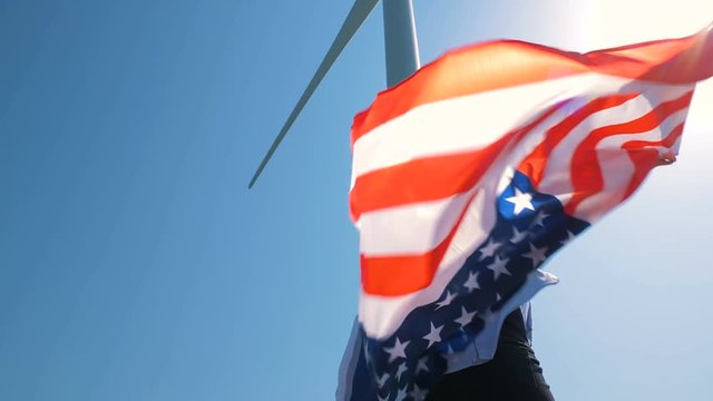 Native American girl with flag with stars and stripes near giant windmills in the field. Love to your country. Celebrating 4th July Independence Day. 4K in slow motion. American dream.