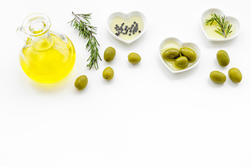 Fresh olive oil in glass jar near green olives and branch of rosemary on white background top view copy space