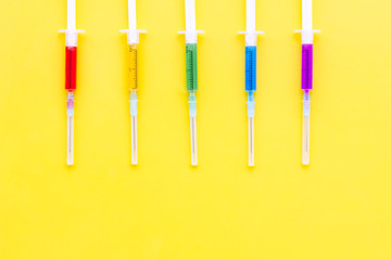Vaccination, immunization. Syringe with colored medicament on yellow background top view copy space