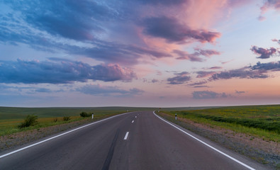 Empty asphalt road through the beautiful field on sunset